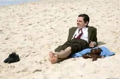 a man sitting on the beach with his feet up in the sand next to a teddy bear