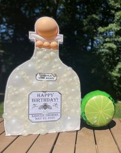 a bottle of birthday soap next to a green ball on a wooden table with trees in the background