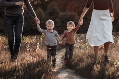 a woman and two children walking down a path in the grass with their hands held by each other