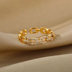 a gold bracelet with white stones on top and an open chain at the bottom, sitting on a beige fabric