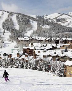 a person riding skis on top of a snow covered slope in front of buildings