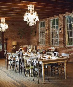 a dining room table set with white chairs and chandelier hanging from the ceiling