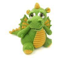 a crocheted green and yellow dragon stuffed animal sitting on a white surface with eyes wide open