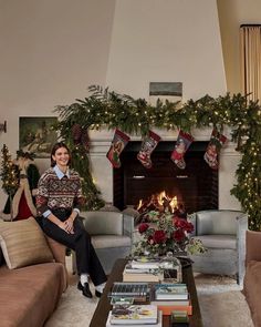 a woman sitting on a couch in front of a fire place with christmas stockings hanging over it