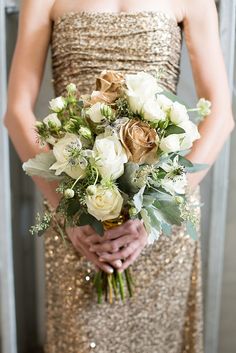 a woman in a gold dress holding a bouquet of white and green flowers on her wedding day