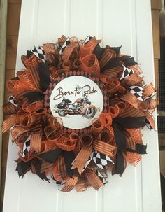 an orange and black wreath with the words born to ride on it is hanging on a white door