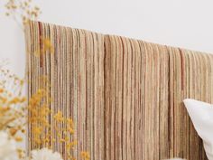 a striped wall hanging next to a bed with white pillows and yellow flowers in the foreground