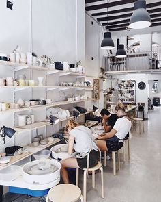 two women sitting at tables in a pottery shop with shelves full of pots and pans