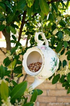 a bird feeder hanging from a tree filled with flowers