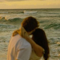 a man and woman standing next to each other in front of the ocean at sunset