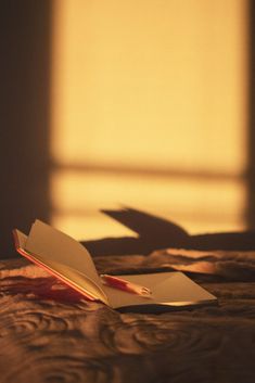 an open book sitting on top of a bed next to a window with light coming in