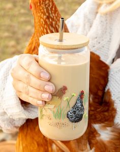 a close up of a person holding a cup with a rooster on it and a chicken in the background