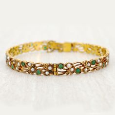 Rendered in yellow gold includes lustrous seed pearl and round cut emeralds. A delightful Art Nouveau design. Gemstone Details: Yellow Gold Seed Pearls Round Emeralds Total carat weight: 1.26 Emerald and Seed Pearl Bangle available at Burdeen's Jewelry. We have many unique offerings of fine estate jewelry listed on our Etsy store. Consider browsing all styles. Call us today for any questions 847-459-8980! *STAY IN THE LOOP* Follow us on Instagram to see our newest pieces! @BurdeensEstate For Eng Yellow Gold Jeweled Bracelet For Formal Occasions, Jeweled Yellow Gold Bracelets For Formal Occasions, Yellow Gold Jeweled Bracelets For Formal Occasions, Elegant Jeweled Yellow Gold Bracelet, Formal Yellow Gold Jeweled Bracelets, Vintage Yellow Gold Pearl Bracelet For Wedding, Vintage Green Bangle For Wedding, Elegant Pearl And Gemstone Wedding Bracelet, Victorian Gold Emerald Jewelry