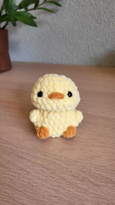 a small crocheted chicken sitting on top of a wooden table next to a potted plant