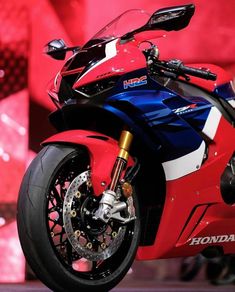 a red and blue motorcycle on display in front of a large screen with the words honda written on it