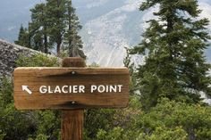 a wooden sign pointing to glacier point on the side of a mountain with pine trees in the background