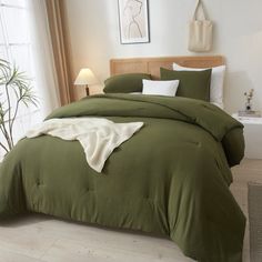 a bed with green comforter and pillows in a white room next to a window