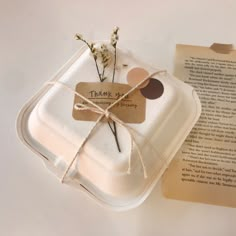 an open book with a tag tied to it next to a flower in a glass container