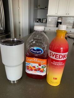 two bottles of orange juice and a cup on a kitchen counter