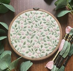 a close up of a embroidery on a wooden surface with flowers and leaves around it