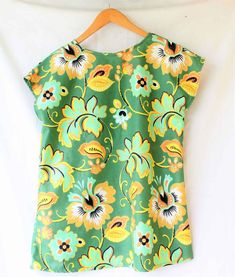 a green top with yellow flowers on it hanging from a wooden hanger next to a white wall