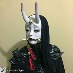 a person wearing a white mask with horns on their head and long black hair is standing in front of a wall