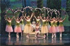 a group of ballerinas standing on stage with their arms in the air