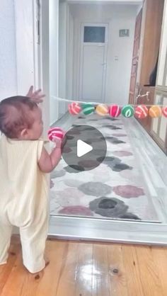 a baby standing on top of a wooden floor next to a glass door with candy