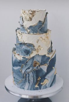 a three tiered cake with blue and gold marbled icing on a silver plate