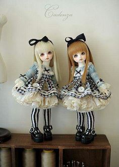 two dolls sitting on top of a wooden shelf