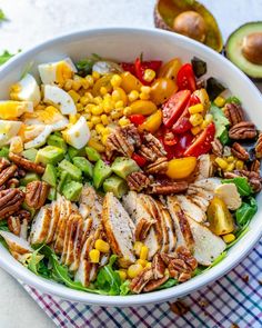 a white bowl filled with chicken, vegetables and hard boiled eggs on top of a checkered table cloth