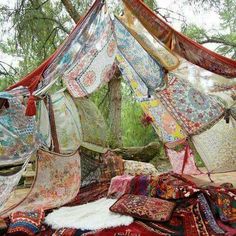 a bed covered in lots of different types of blankets and rugs next to a tree