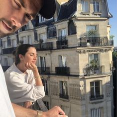 a man and woman standing next to each other looking at their cell phones in front of a building