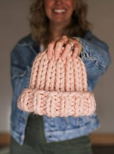 a woman holding up a pink knitted object