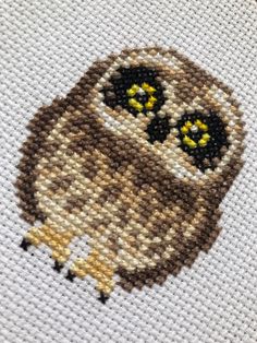 an owl cross stitched on to a white piece of cloth with yellow eyes and black ears