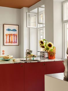 a kitchen with sunflowers on the window sill and an art piece in the corner