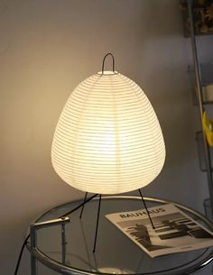 a white lamp sitting on top of a table next to a magazine and some shelves