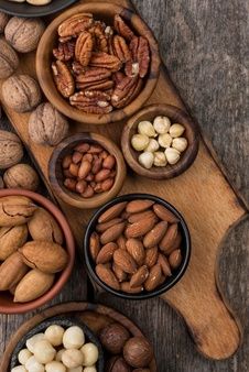 nuts are arranged in bowls on a wooden board, including walnuts and pistachios