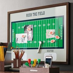 a football field is mounted on the wall above a desk with pens, pencils and markers