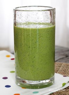 a glass filled with green liquid sitting on top of a wooden table next to a polka dot napkin