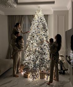 three people standing around a white christmas tree