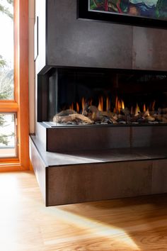 a fire place in the middle of a room with wood flooring and large windows