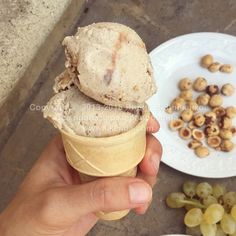 someone holding an ice cream cone in front of some grapes and nuts on the table