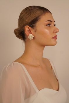 a woman wearing a white dress with a flower in her hair, looking off to the side