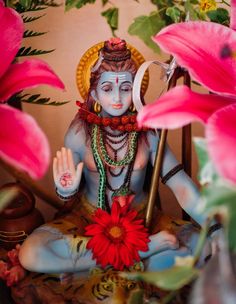 there is a statue of the hindu god sitting in front of pink flowers and holding a stick