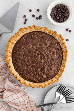 a chocolate pie sitting on top of a table next to a knife and bowl filled with chocolate chips