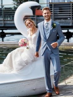 a bride and groom standing on a boat in front of a swan sculpture at the water's edge