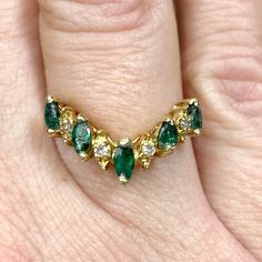 a woman's gold ring with emeralds and diamonds on her finger, set in 18k yellow gold