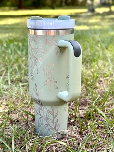 a cup that is sitting on the ground in the grass with its lid open and handle attached to it