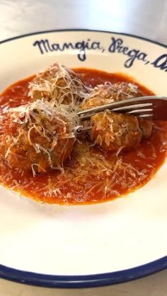 a white plate topped with meatballs covered in sauce and grated parmesan cheese